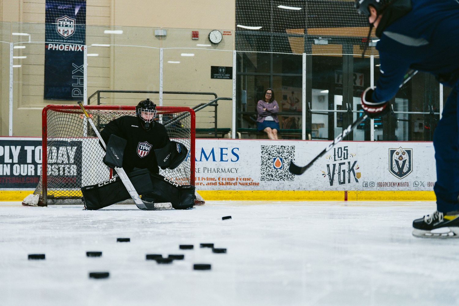 Hockey goalie in black gear prepares to face shots with pucks lined up during TPH ice hockey practice.