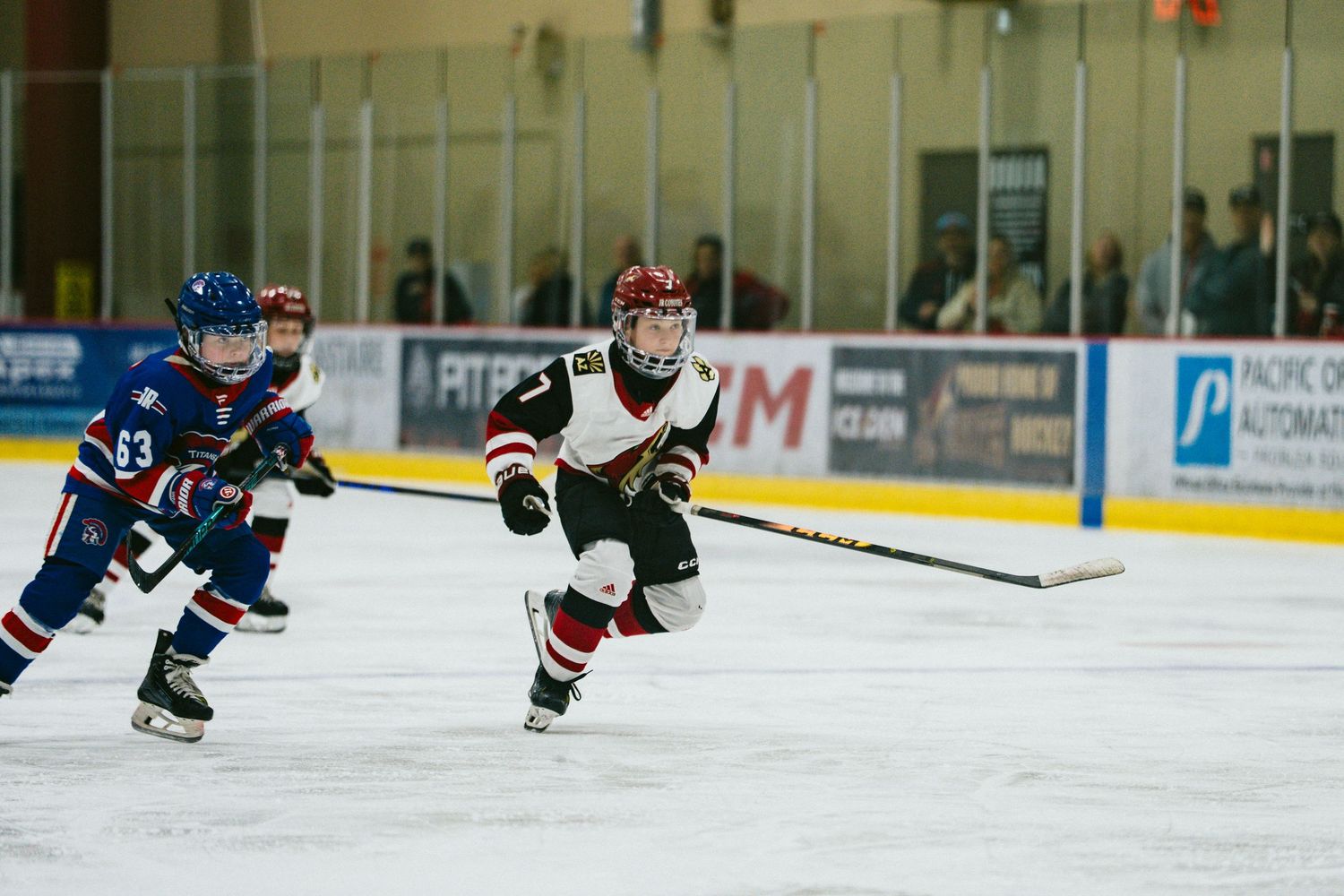 Ice hockey players chase after the puck during a competitive game on a brightly lit indoor rink.