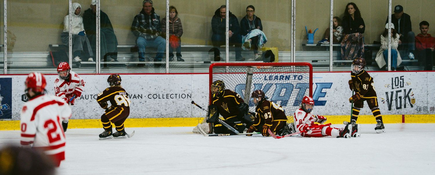 Wide view of ice hockey rink showing players in action with spectators watching from stands.
