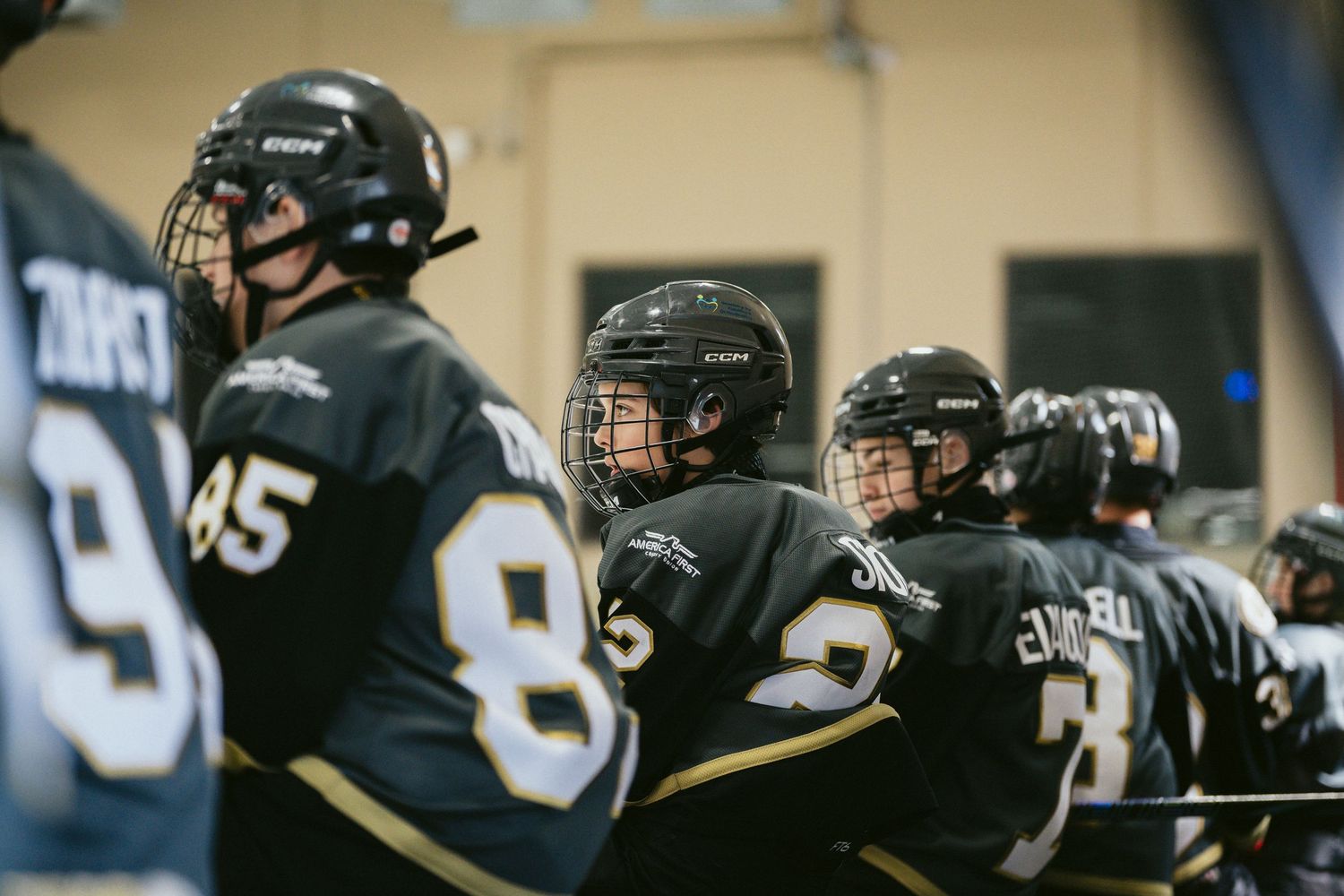 Hockey players in black jerseys lined up along the bench during a game.