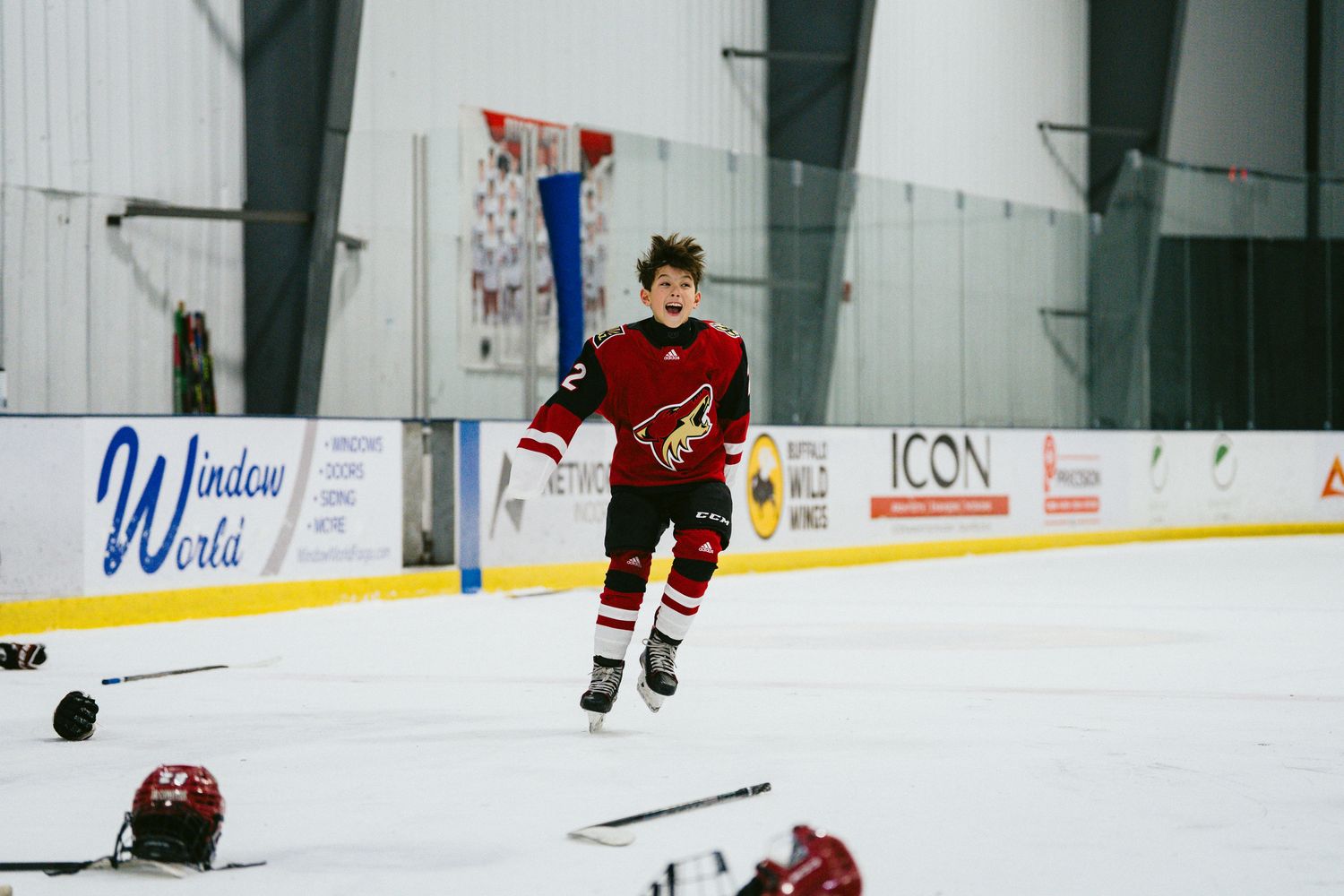 Hockey players practicing drills on indoor ice rink with white walls.