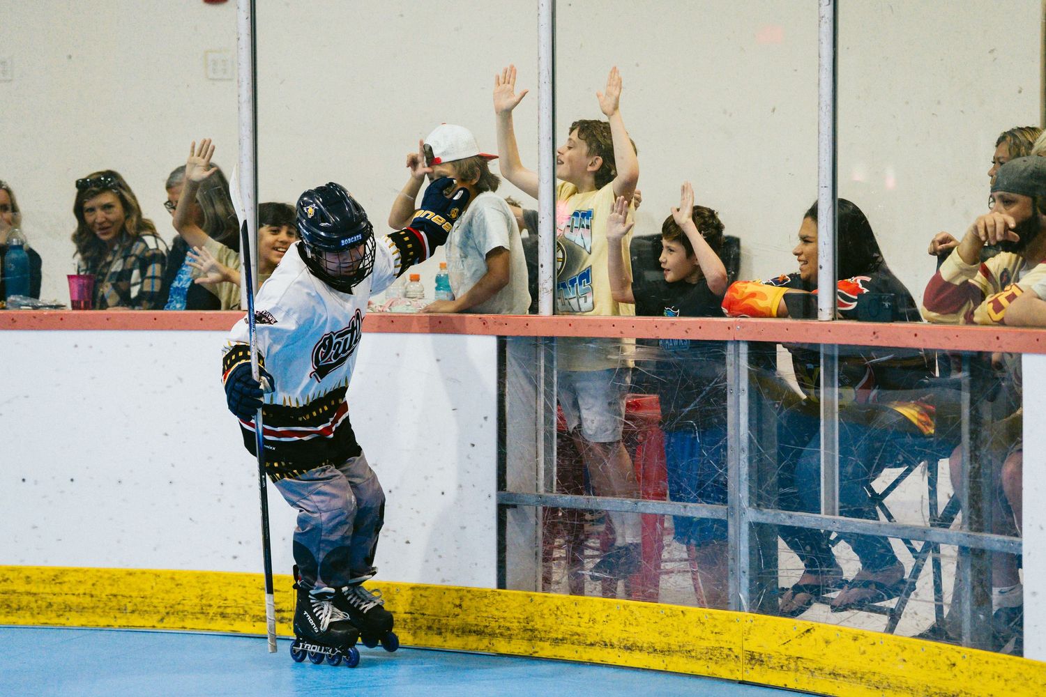 Roller derby player high-fives fans through the rink barrier during an exciting indoor skating event.