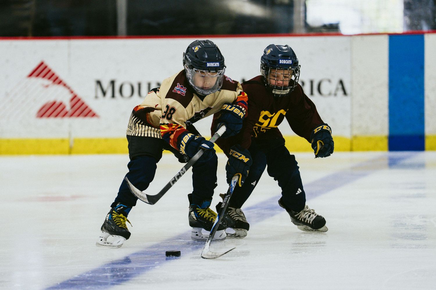 Two young hockey players compete for the puck in an intense youth ice hockey game.