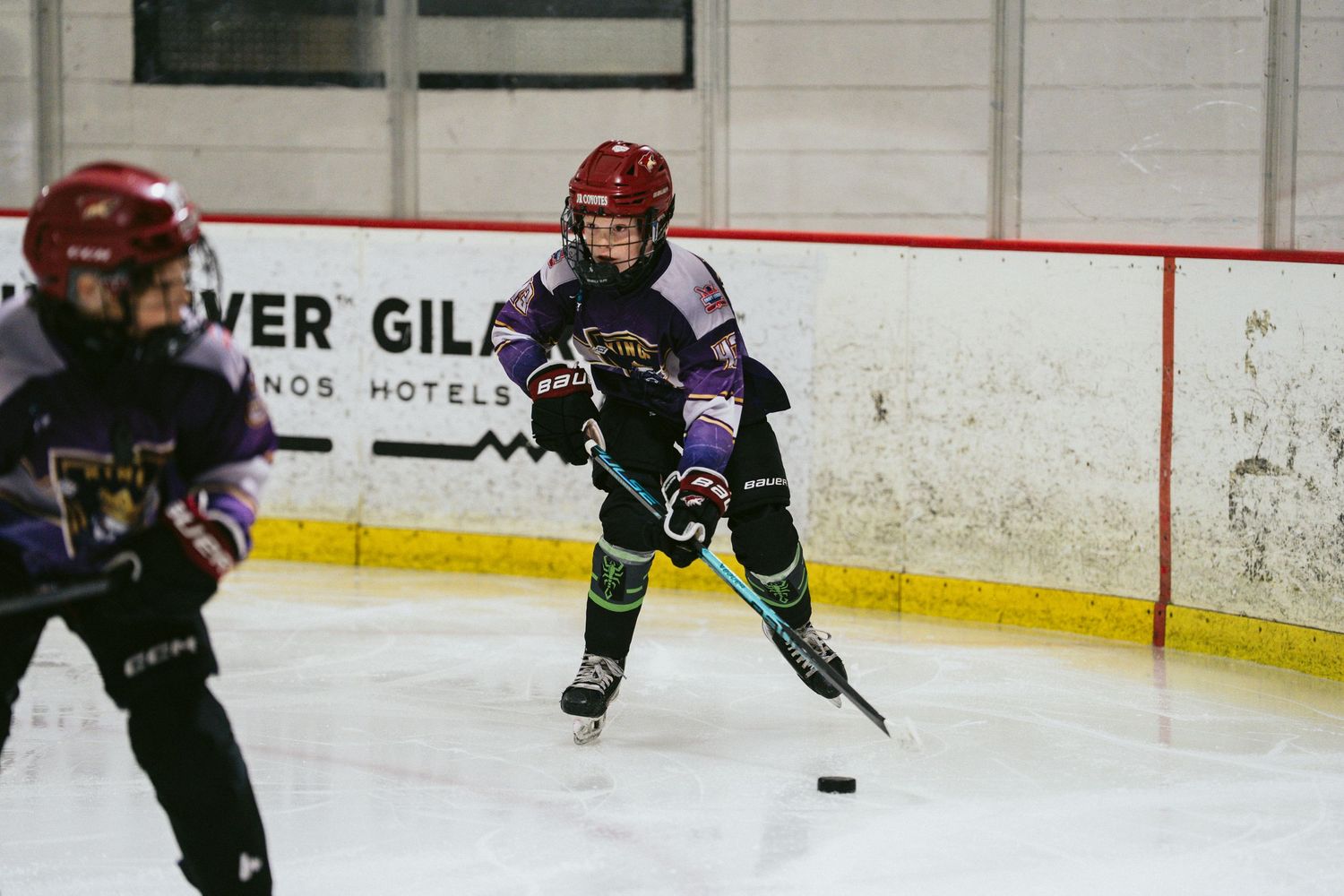 Young hockey player in purple uniform prepares to pass the puck during an indoor youth hockey game.