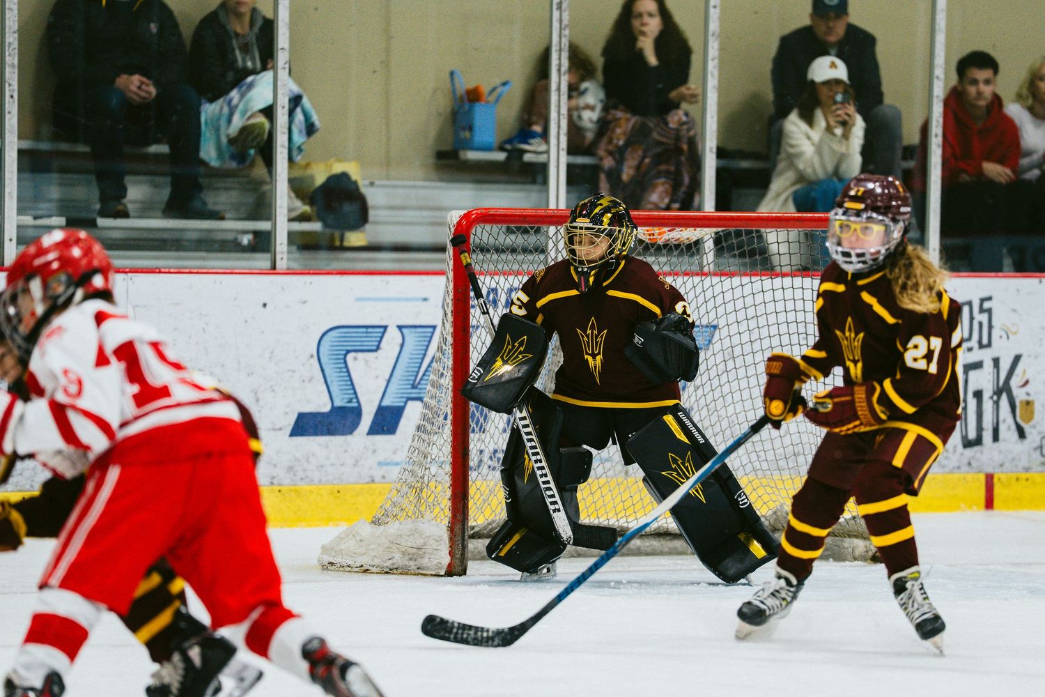 Hockey players in brown and red jerseys face off during an indoor ice hockey match.