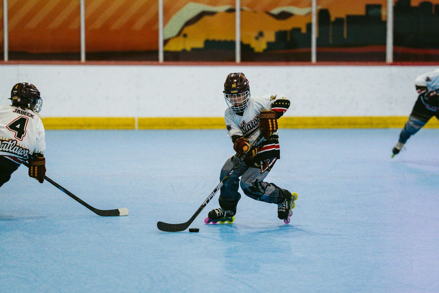 Young hockey players compete in an indoor roller hockey game on a blue rink.