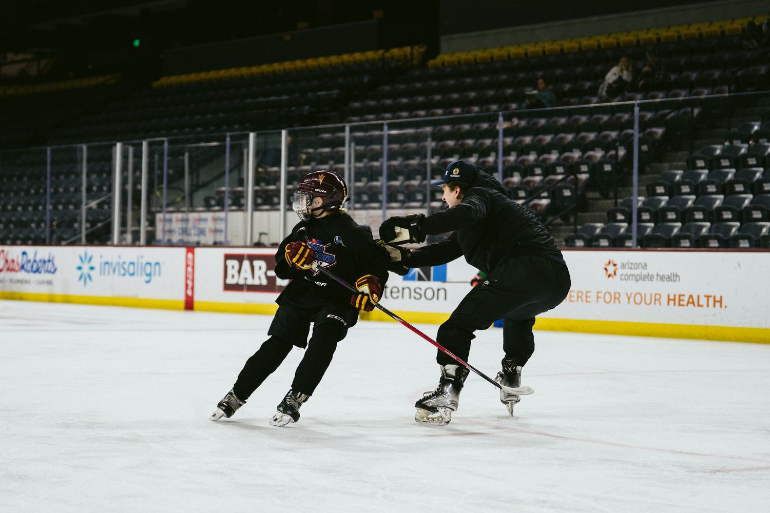 Two hockey players practicing defensive skating and puck control drills at indoor arena.