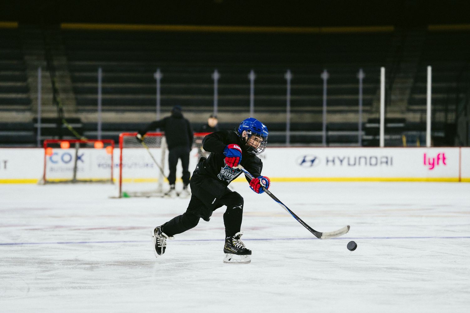 Young hockey player in blue helmet winds up for a shot during an indoor ice hockey practice session.