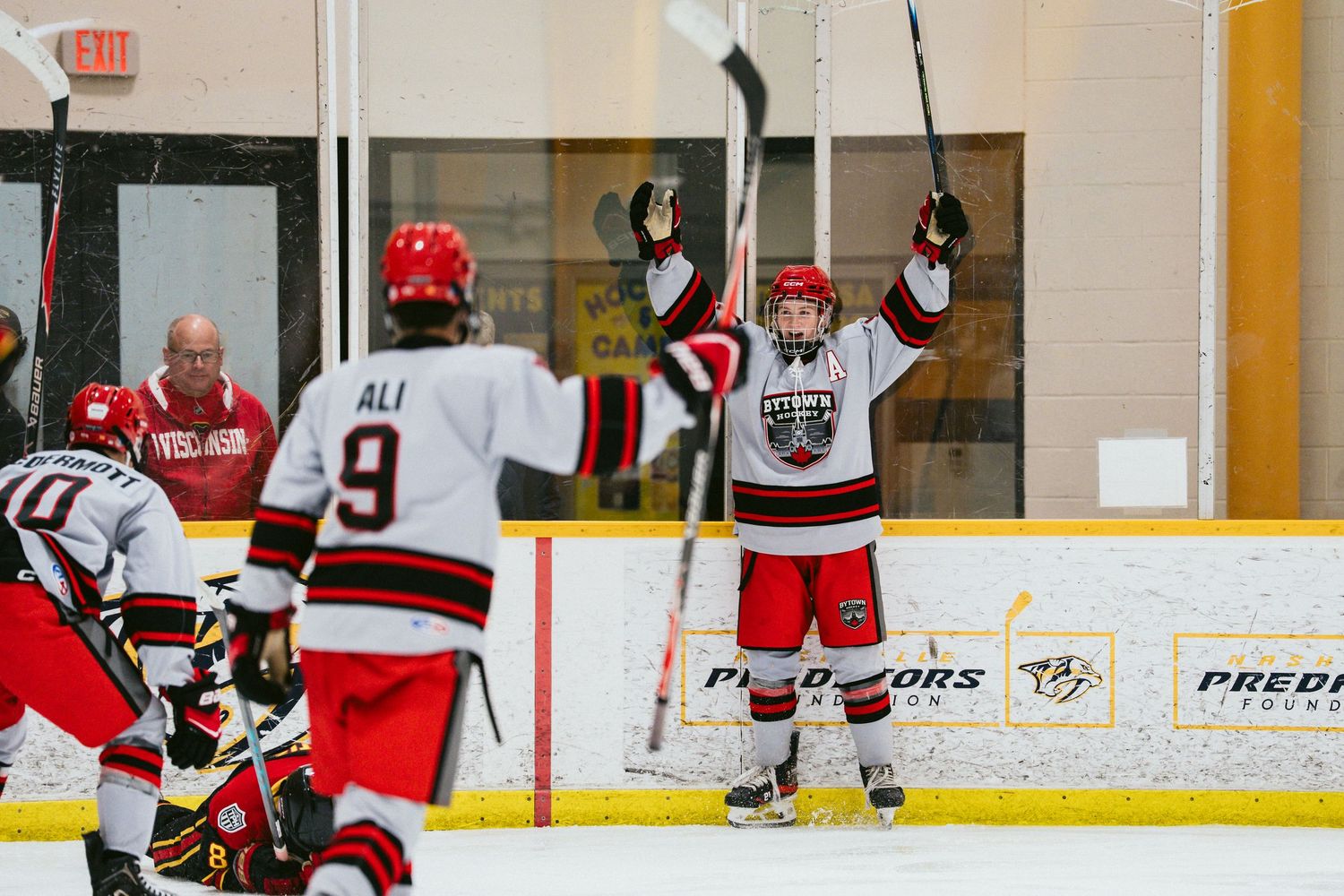 Hockey players in red and white uniforms celebrate a goal on an indoor ice rink during a competitive game.