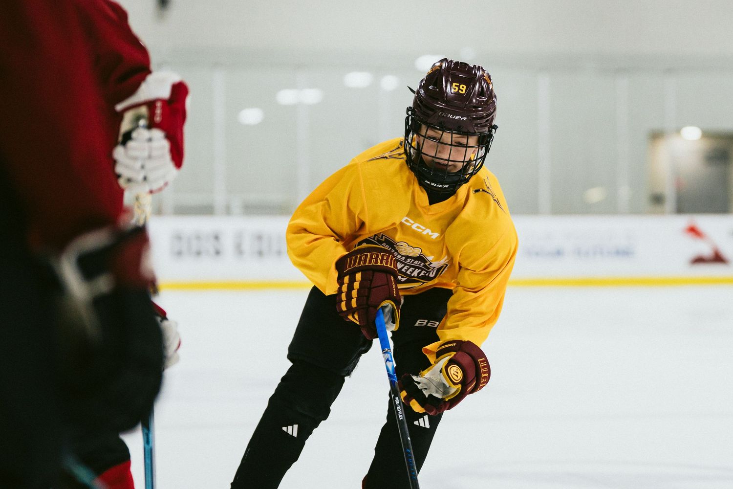 Young hockey player in yellow jersey focuses on puck control during competitive ice hockey practice drill.