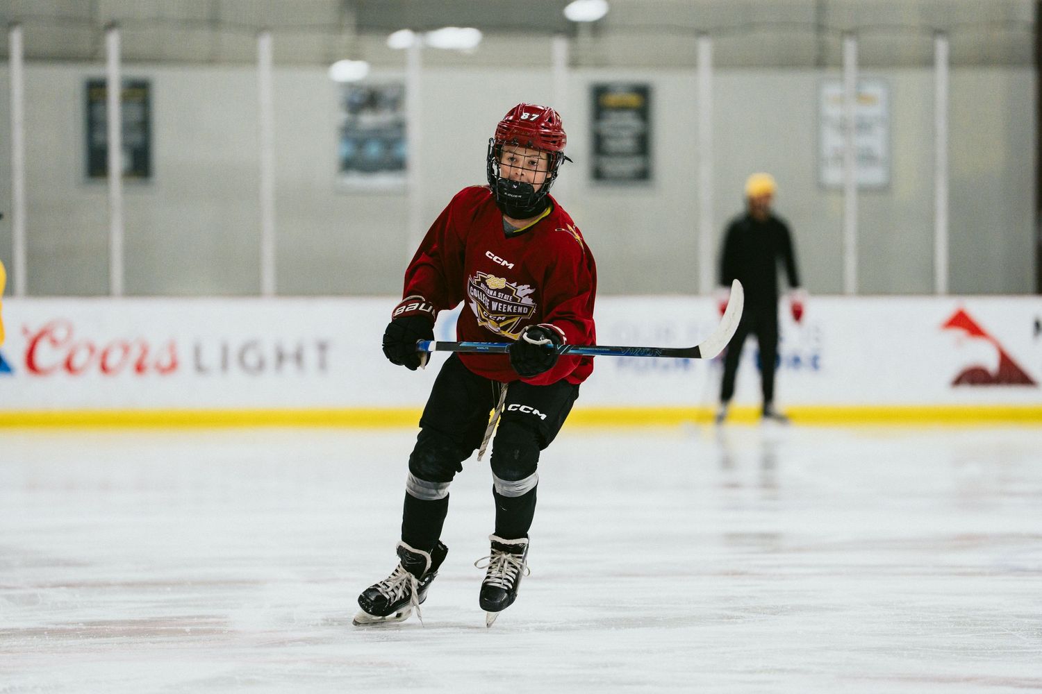 Young hockey player in red jersey skates energetically across indoor ice rink during practice session.