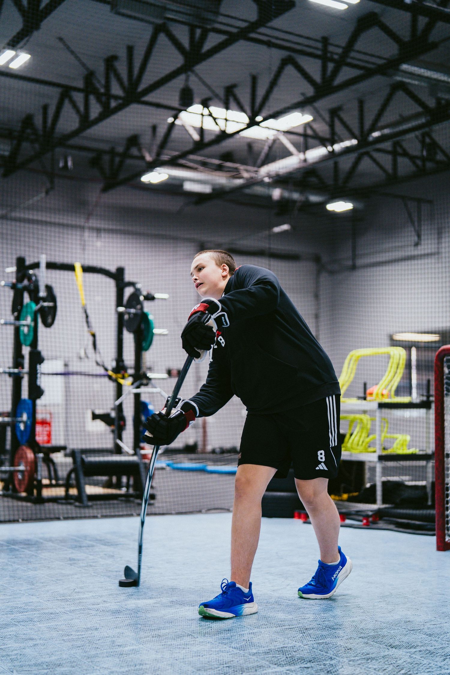 Young athlete practicing hockey stickhandling drills in a modern indoor training facility wearing Adidas gear.