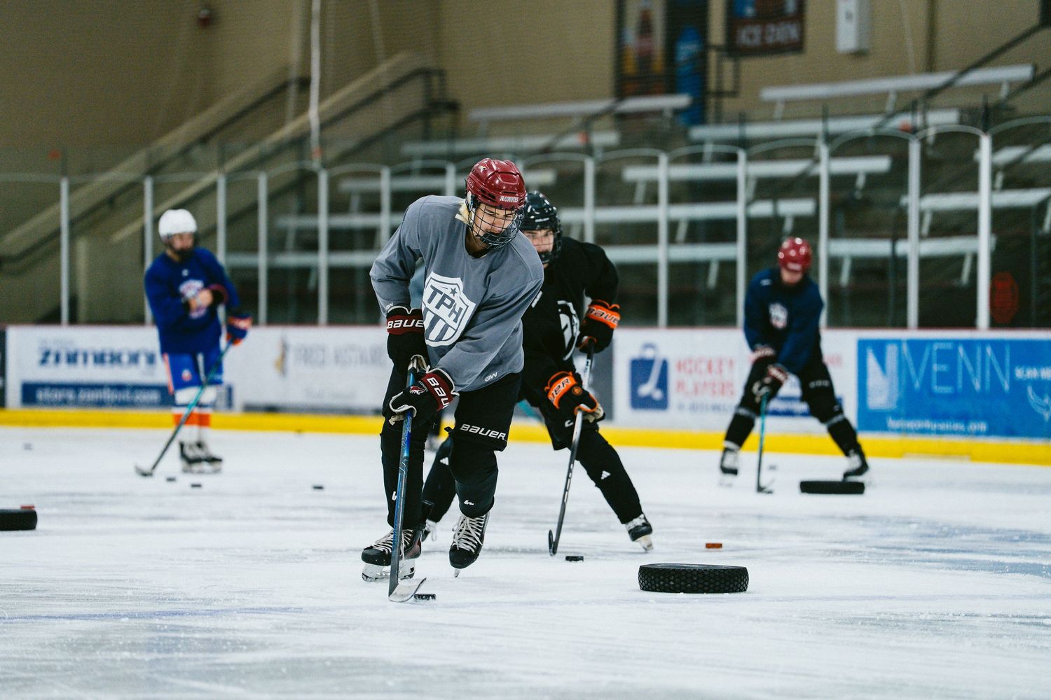 Hockey players skate with pucks during competitive indoor ice rink training drill.