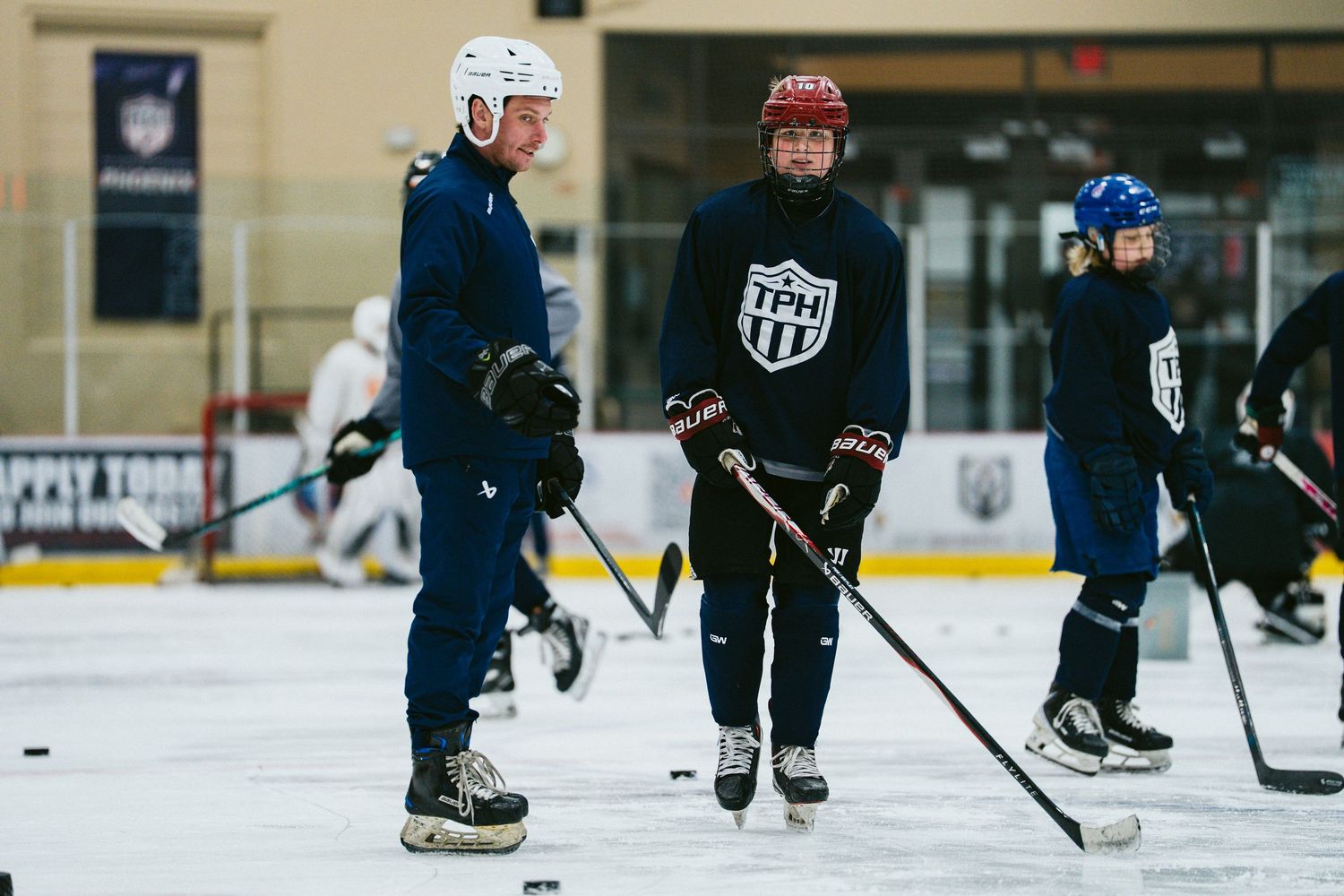Hockey players in TPH jerseys practice skating drills on an indoor ice rink during a training session.