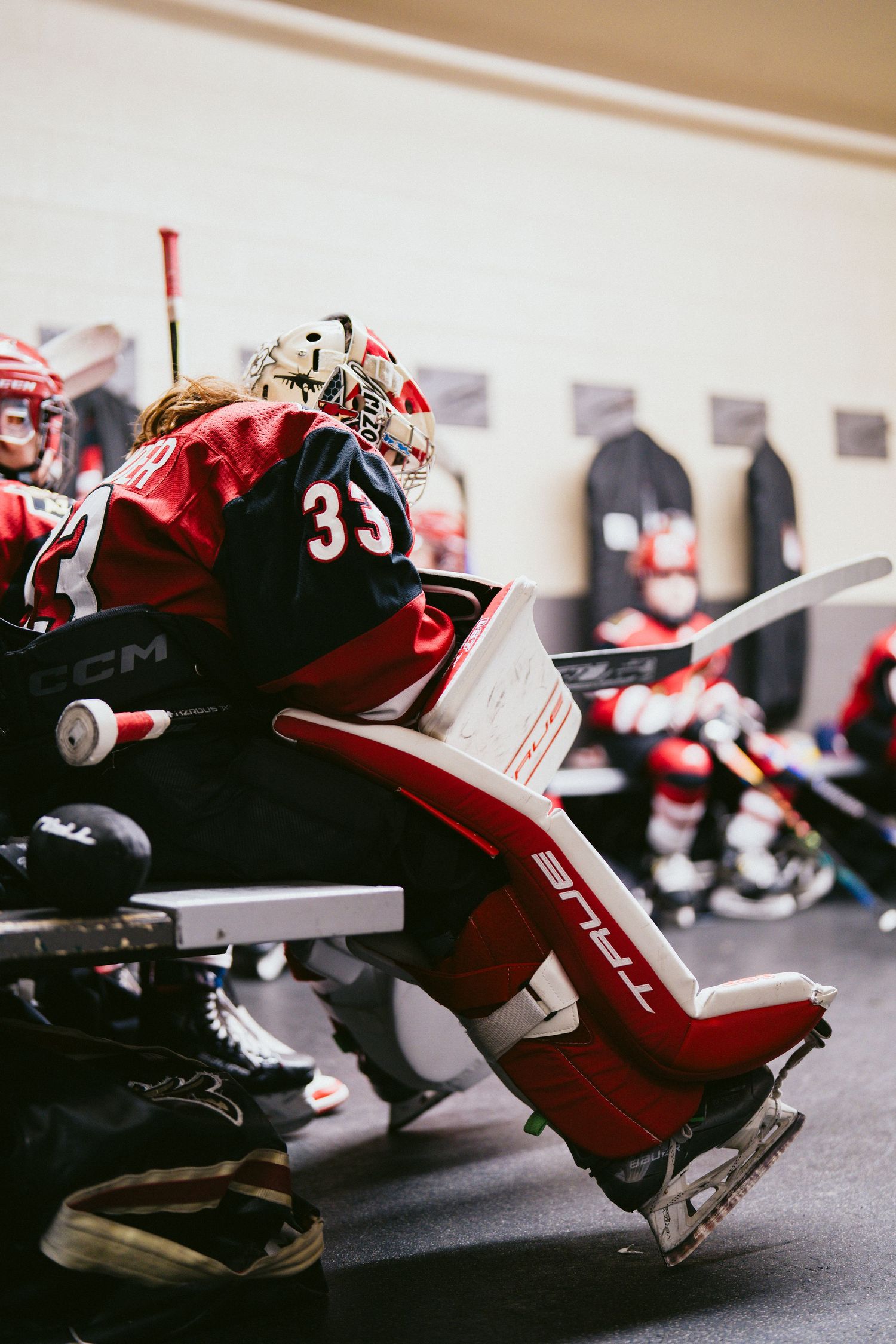 Close-up of hockey goalie equipment showing red and black leg pads with number 33 visible.