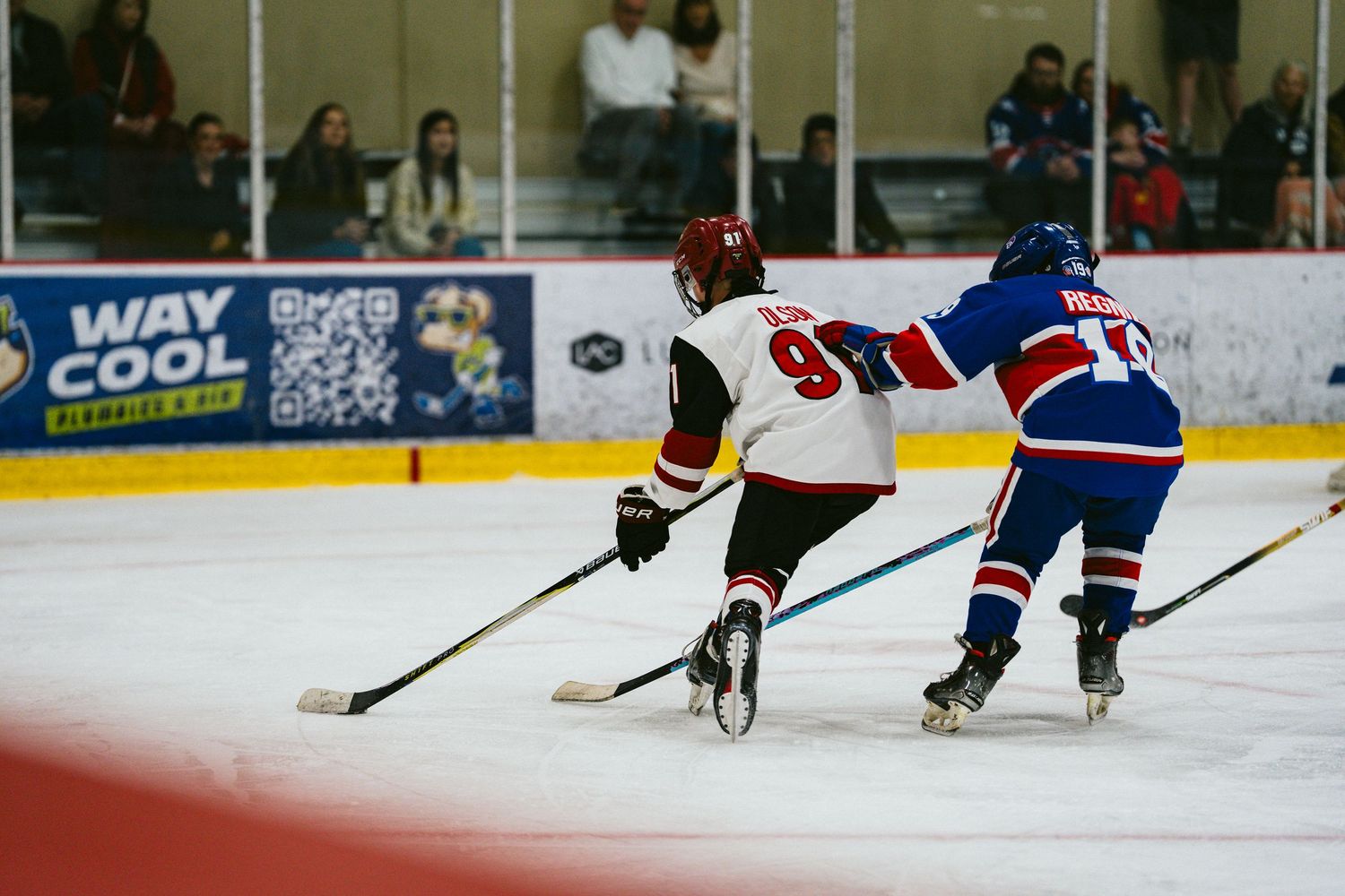 Youth hockey players from opposing teams battle for possession during competitive match.