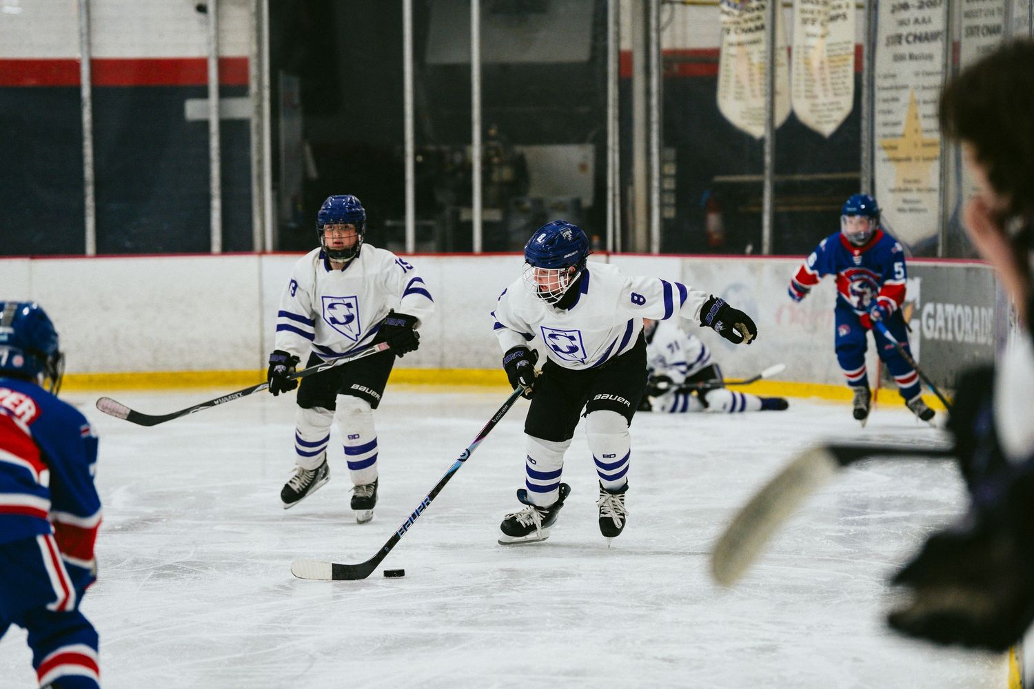 Multiple hockey players in white uniforms skating during game on indoor rink.