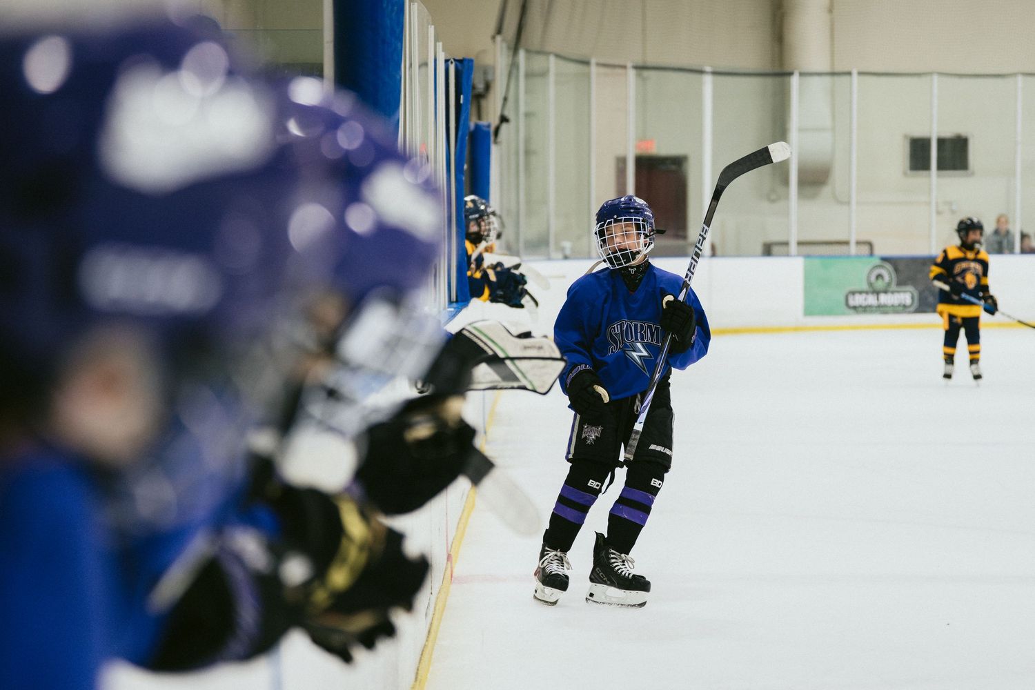 Young hockey players practice skating drills on an indoor ice rink wearing blue helmets and uniforms.
