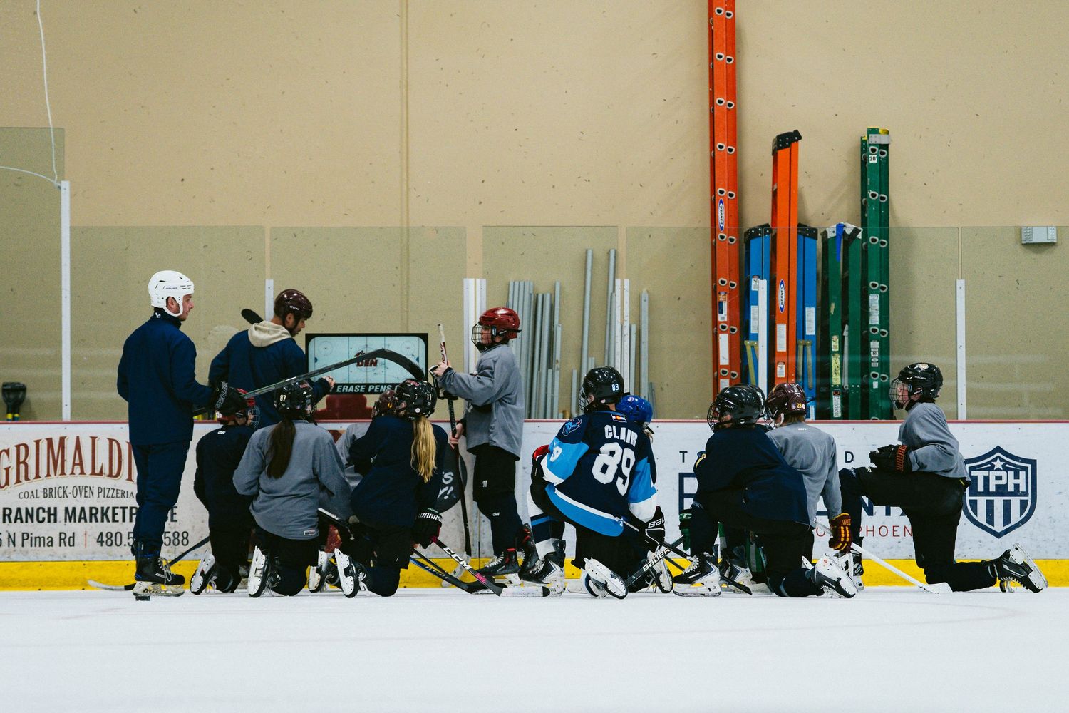 Hockey team huddles around coach on ice rink during an indoor TPH training session practice.