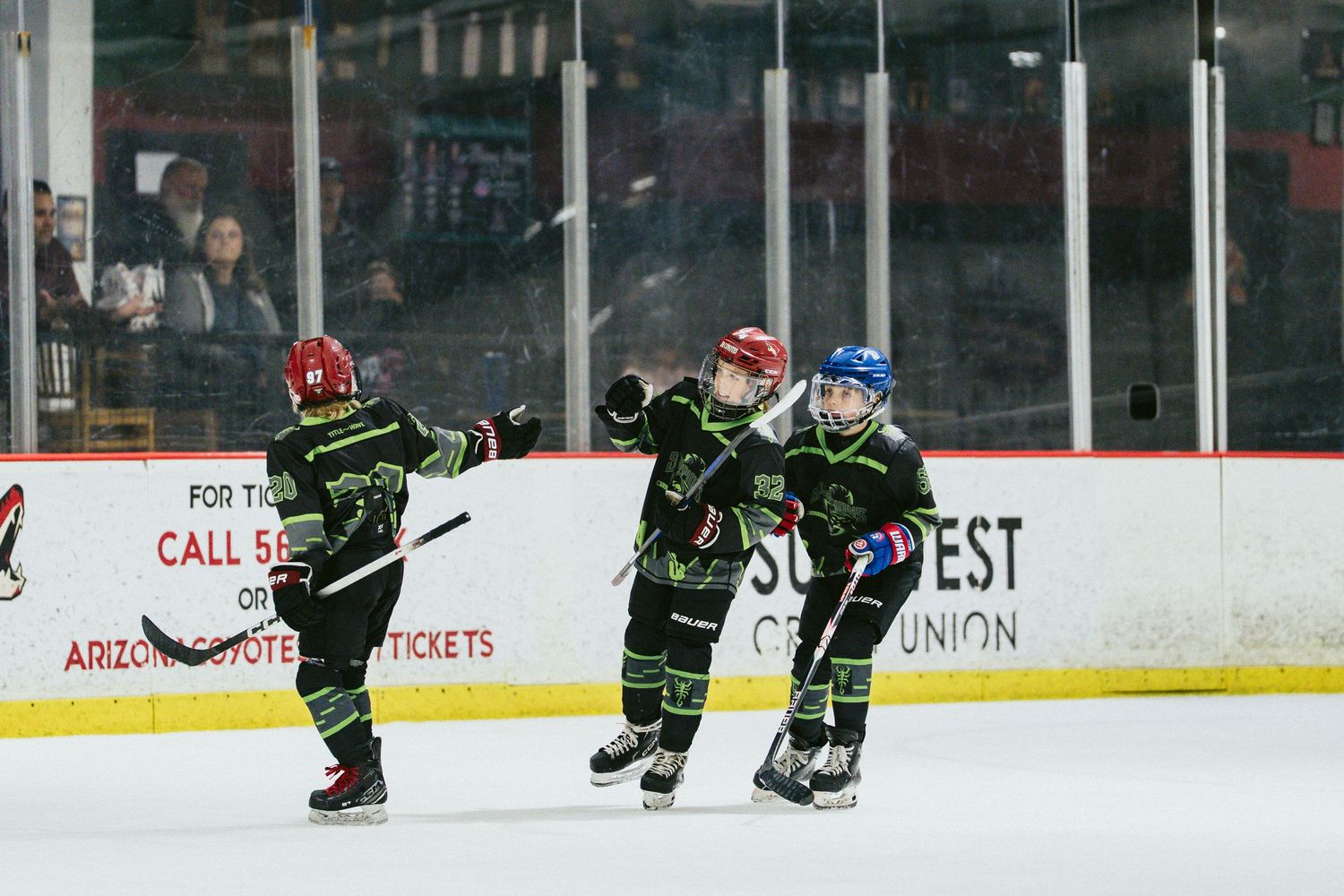 Youth hockey players in green Scorpions uniforms celebrating goal on indoor ice rink.