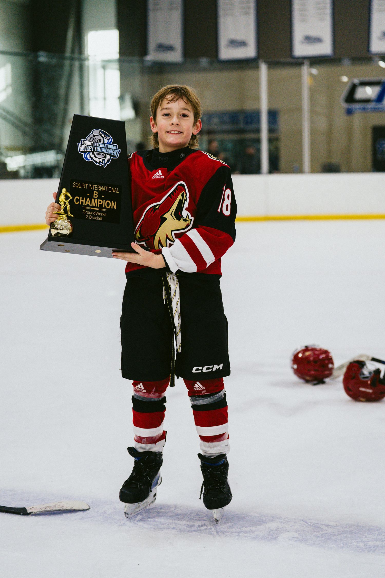 Young hockey player in red uniform proudly shows off award while skating.