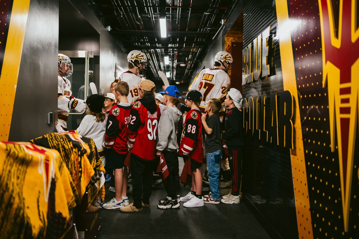 Hockey team walking through a dimly lit tunnel with yellow lighting and decorative elements.
