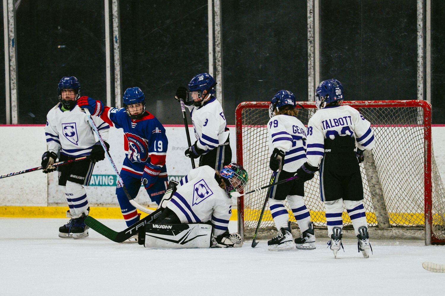Hockey players in blue and white jerseys face off during an intense game on the ice rink.