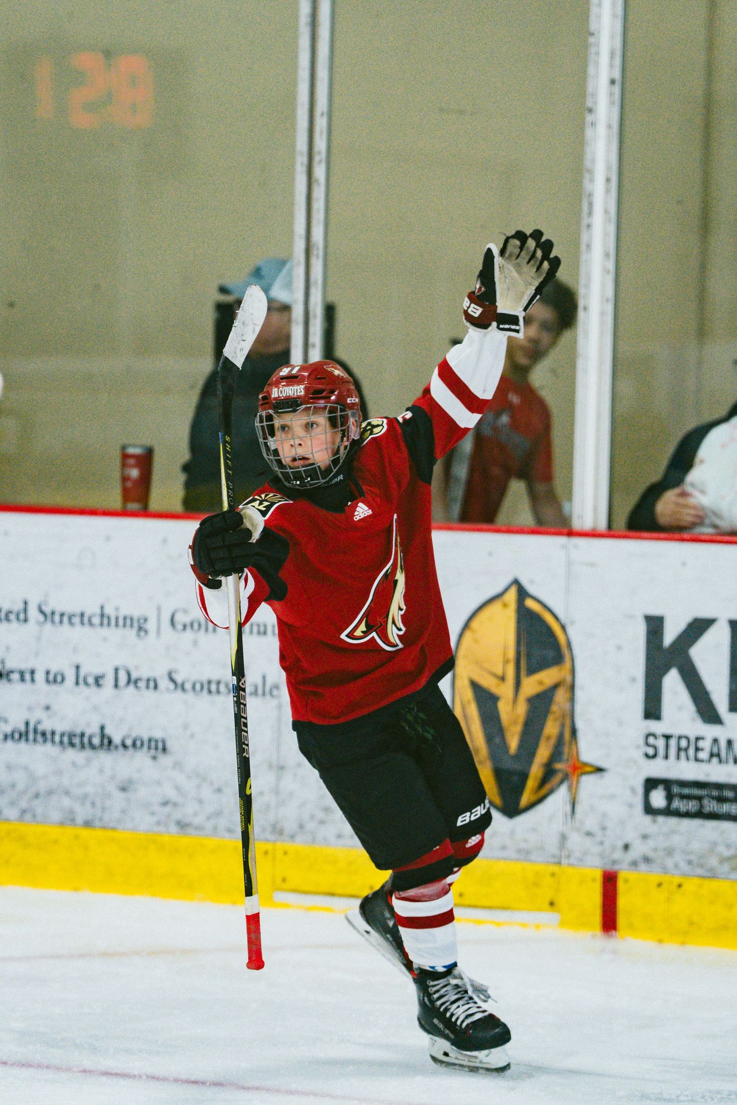 Youth hockey player in red jersey leaps into the air while skating on ice during a game.