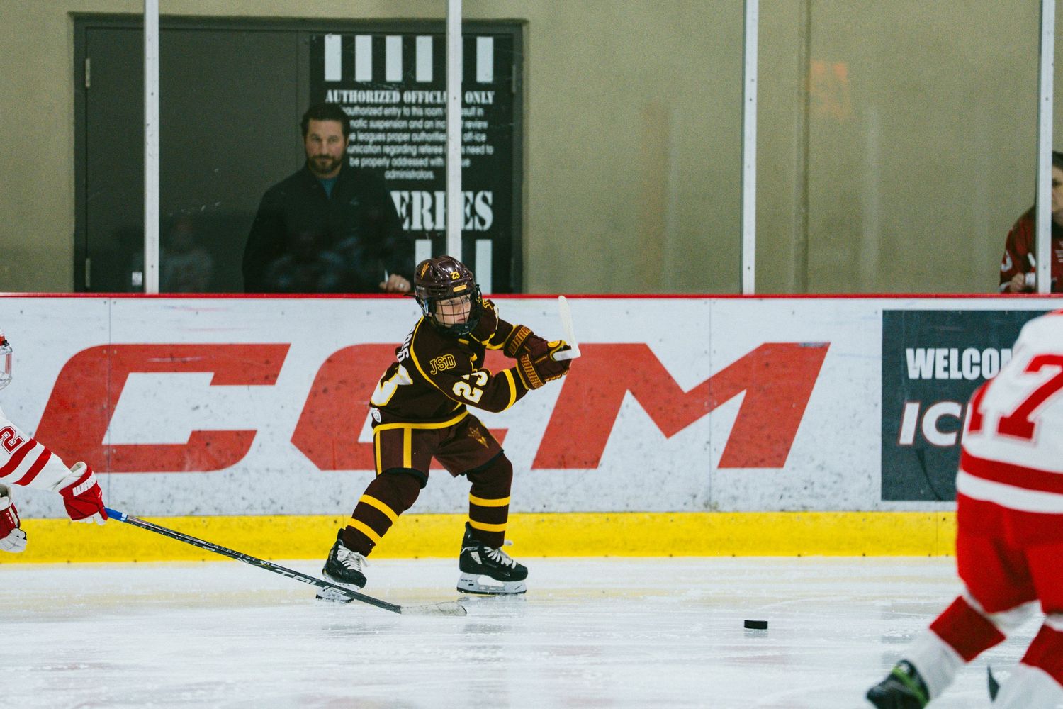 Hockey players skate on ice during a game with visible CCM advertising boards in the background.