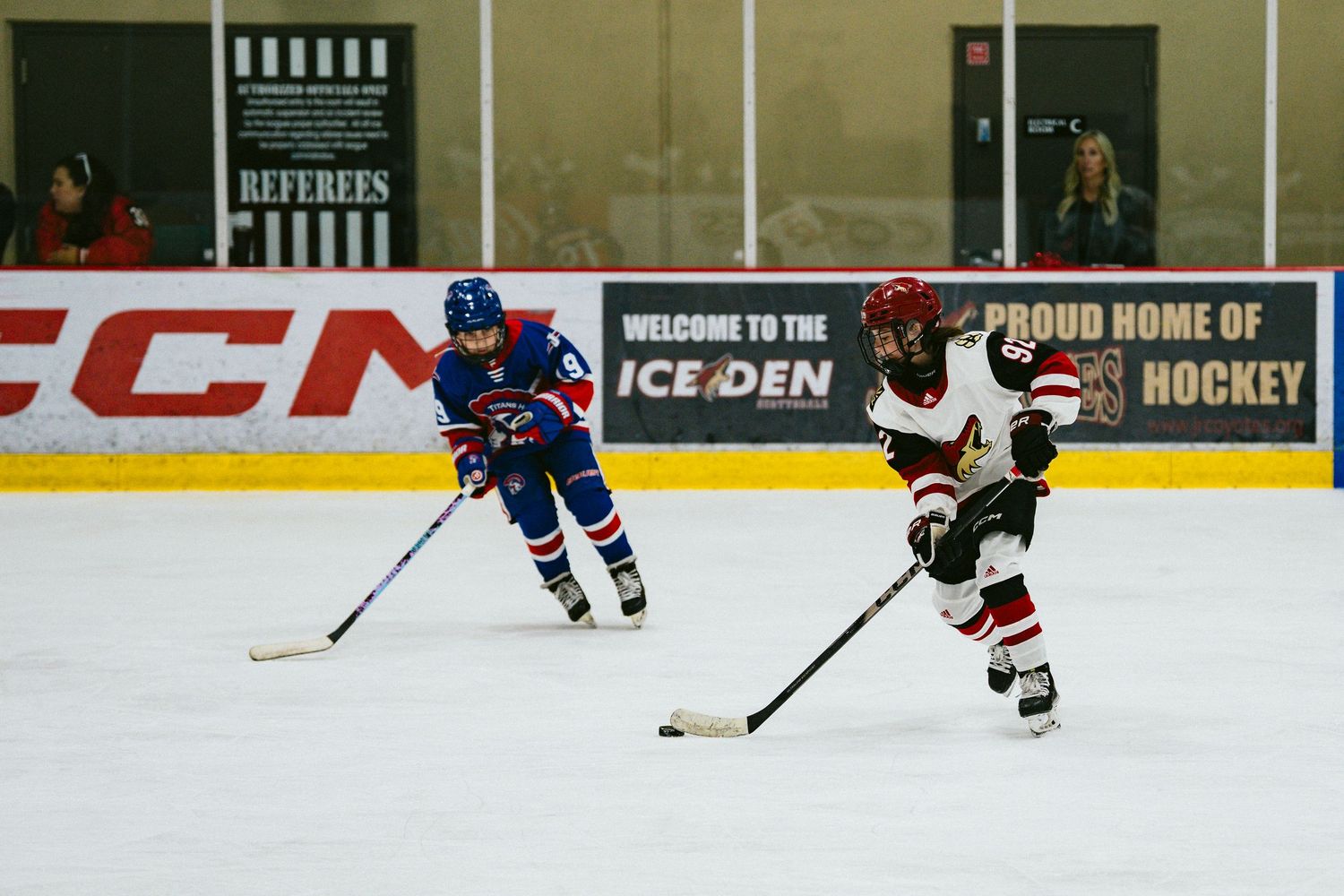 Hockey players maneuver on ice with advertising boards visible along the rink walls.
