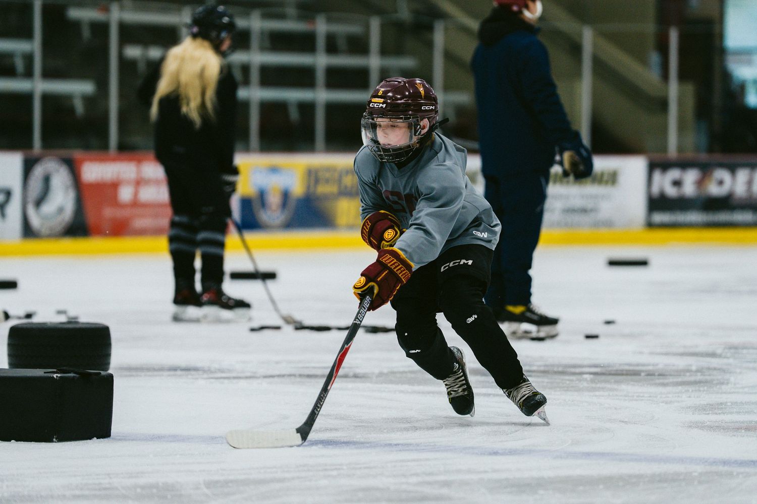 Young child in hockey gear skating and handling a puck on an indoor ice rink during practice.