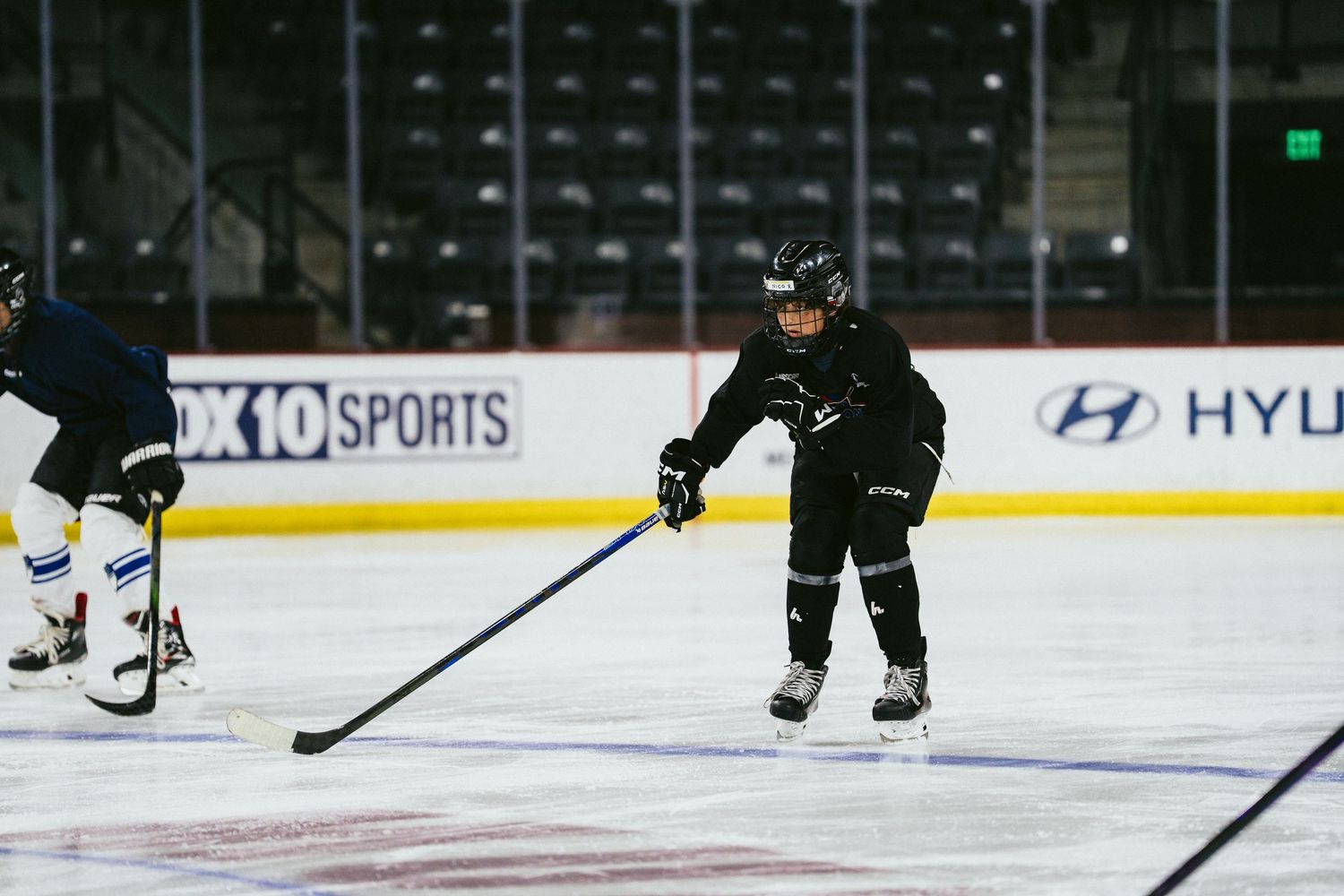 Young hockey player in black uniform handles puck during ice hockey practice in an indoor arena.