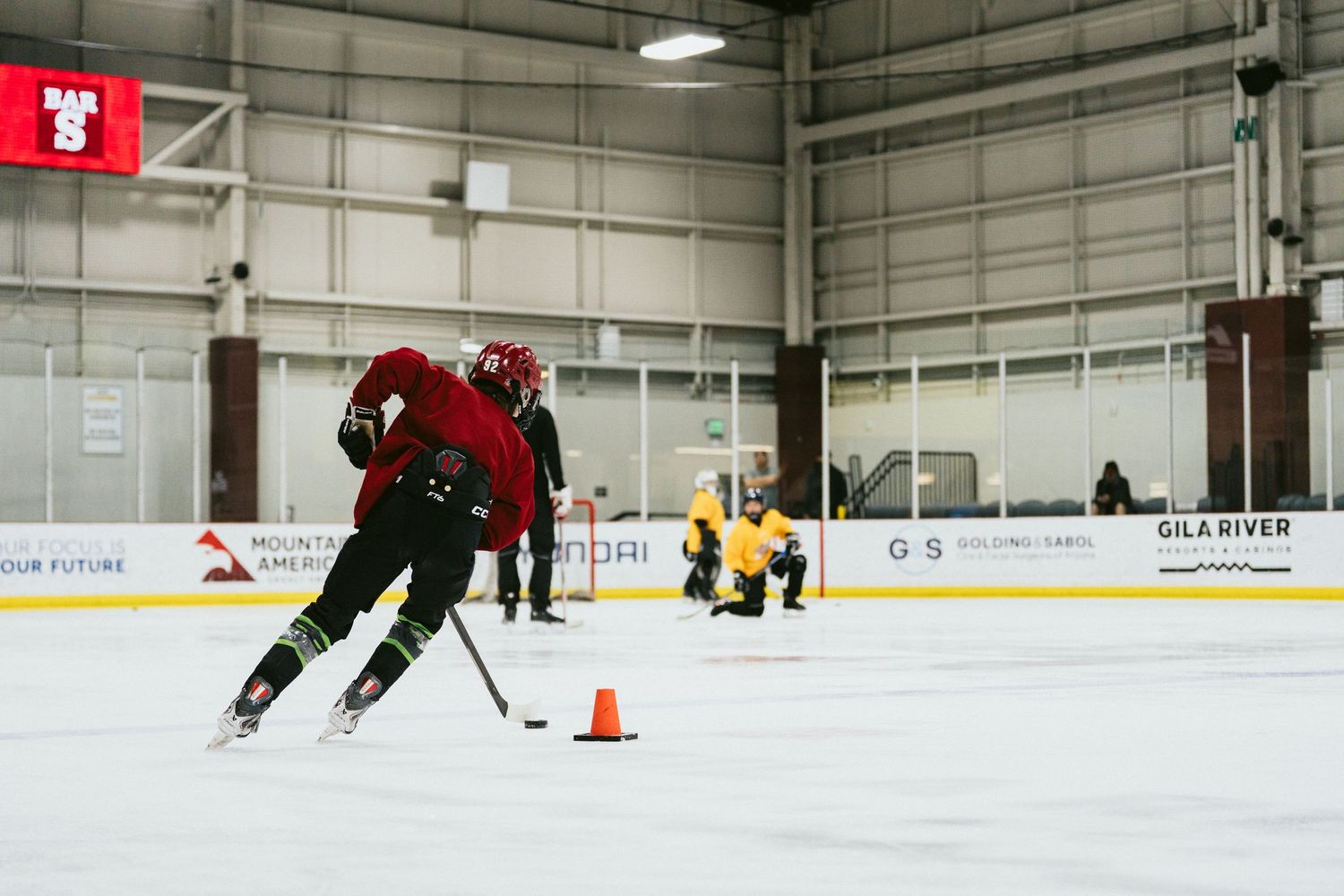 Hockey player skating past orange cone during drill at indoor ice rink practice session.