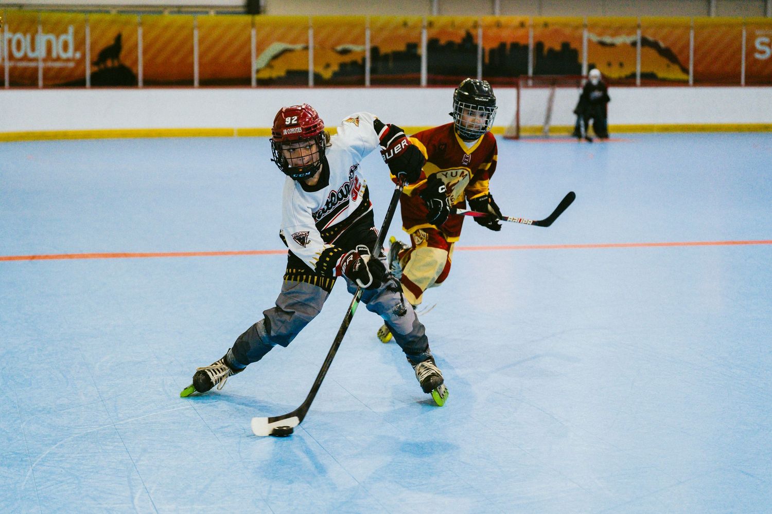 Two young hockey players compete for the puck on an indoor rink during a youth hockey game.