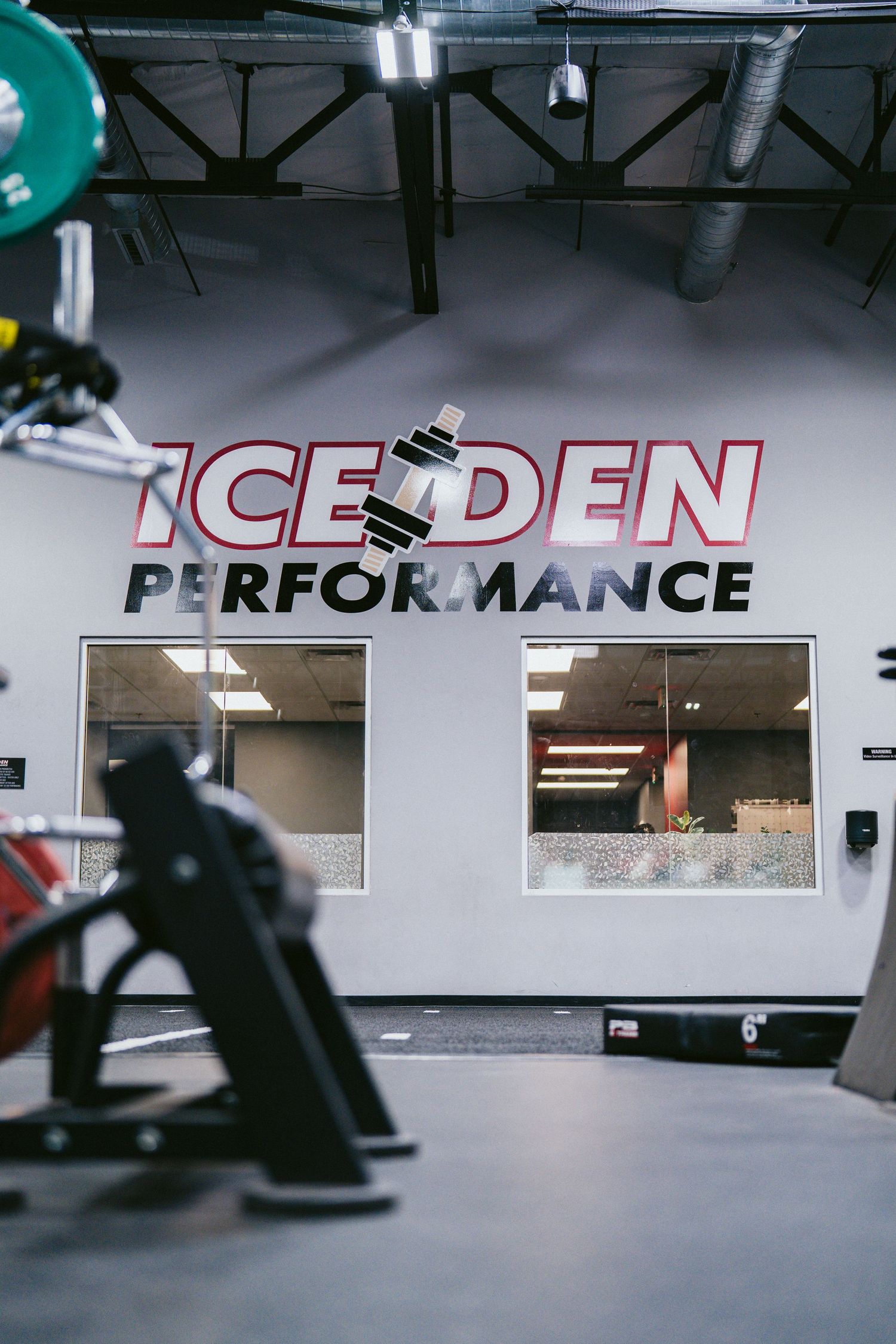 Ice Den Performance gym interior featuring weightlifting equipment and bold branded wall signage.