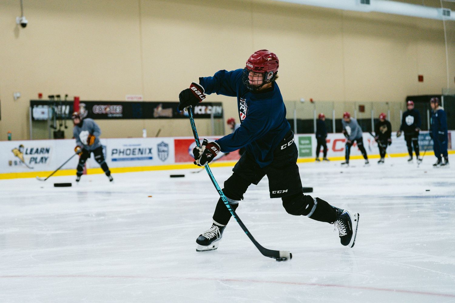 Young hockey player takes powerful shot on ice during indoor hockey training session.