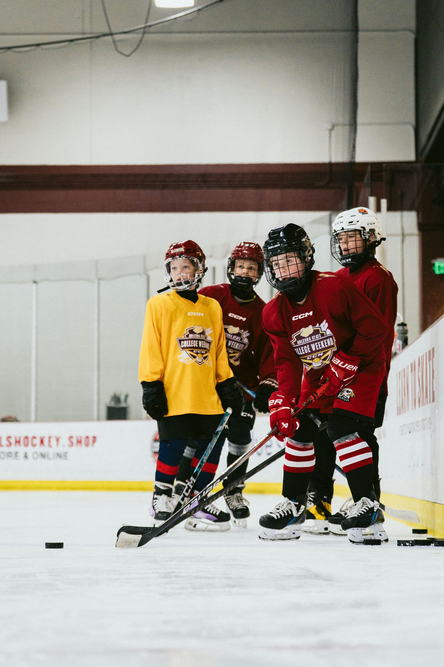 Four young hockey players in red and yellow jerseys stand together on ice rink during team practice.