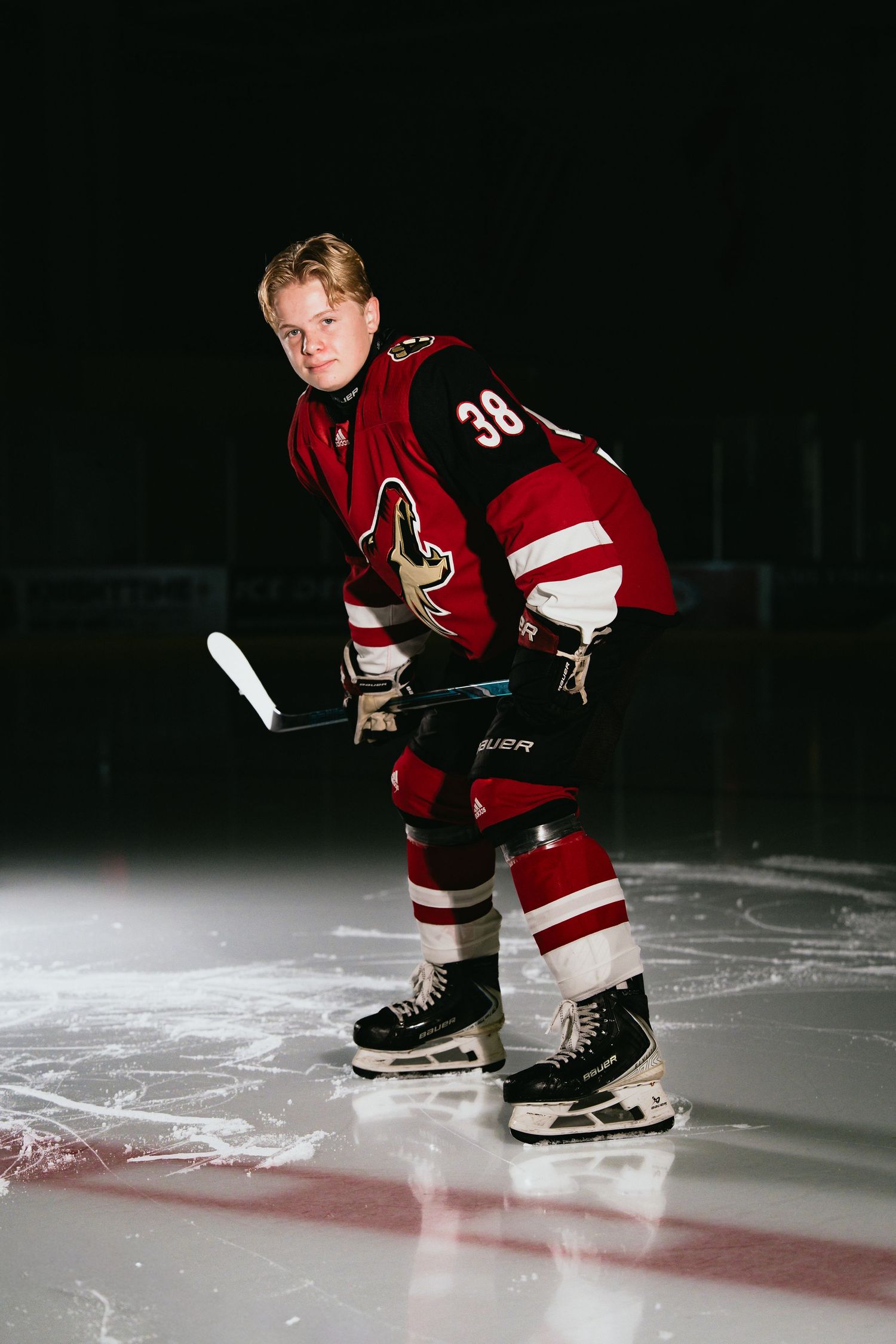 Hockey player in red jersey number 38 skating on ice rink in dark arena.