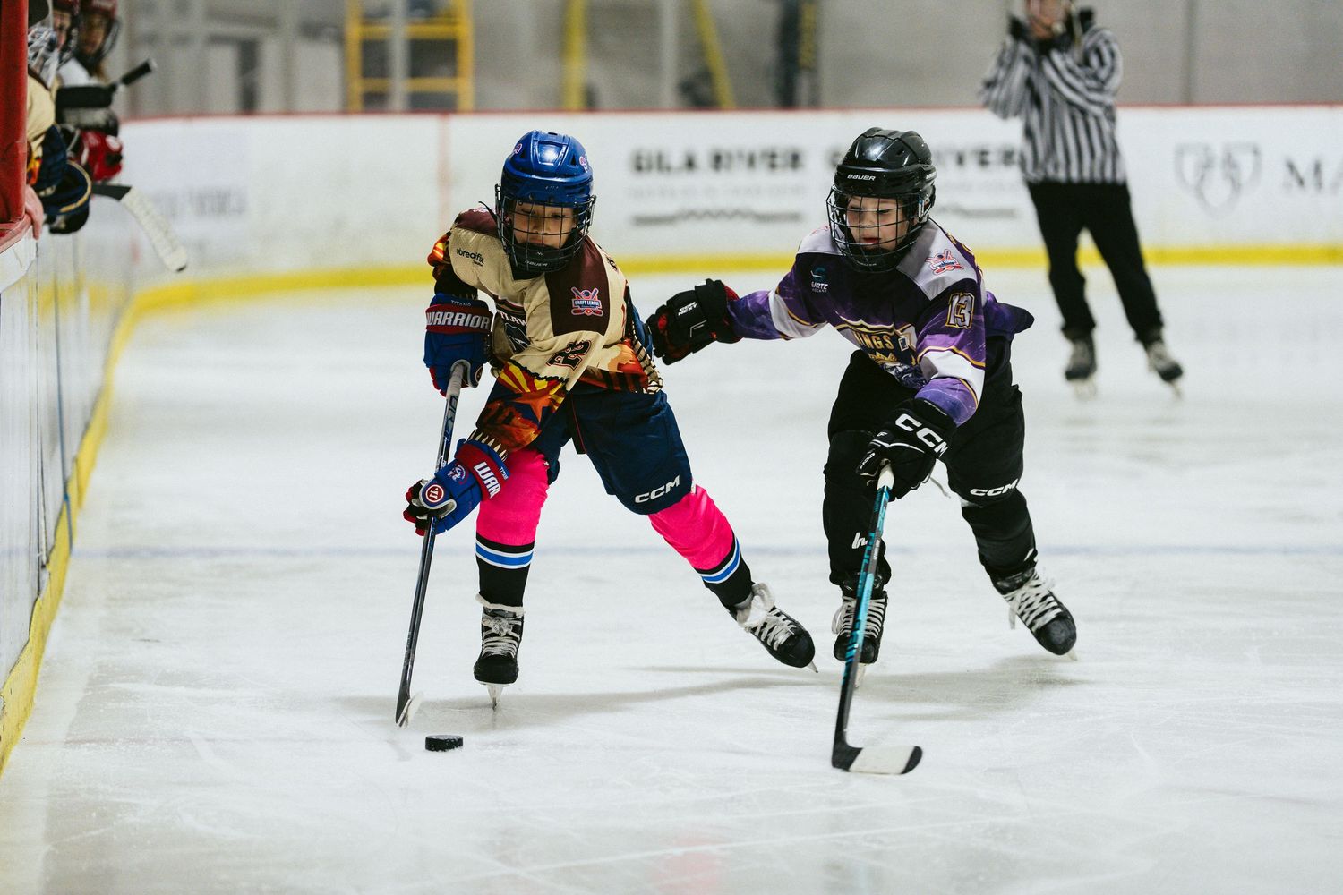 Two young girls compete for the puck during a youth ice hockey game on indoor rink.