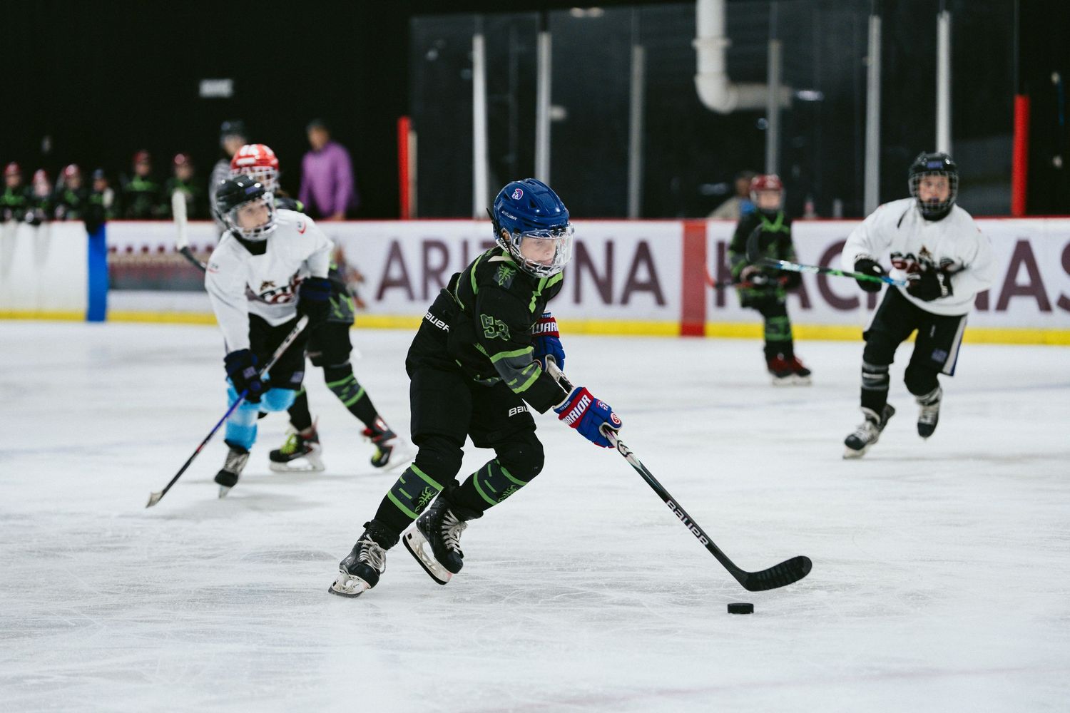 Young hockey player in black uniform skates with puck during youth ice hockey practice or game.