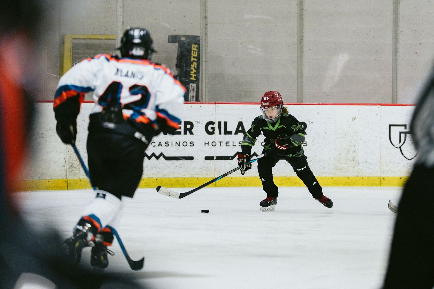 Young hockey players compete on ice during a youth hockey game at an indoor rink.