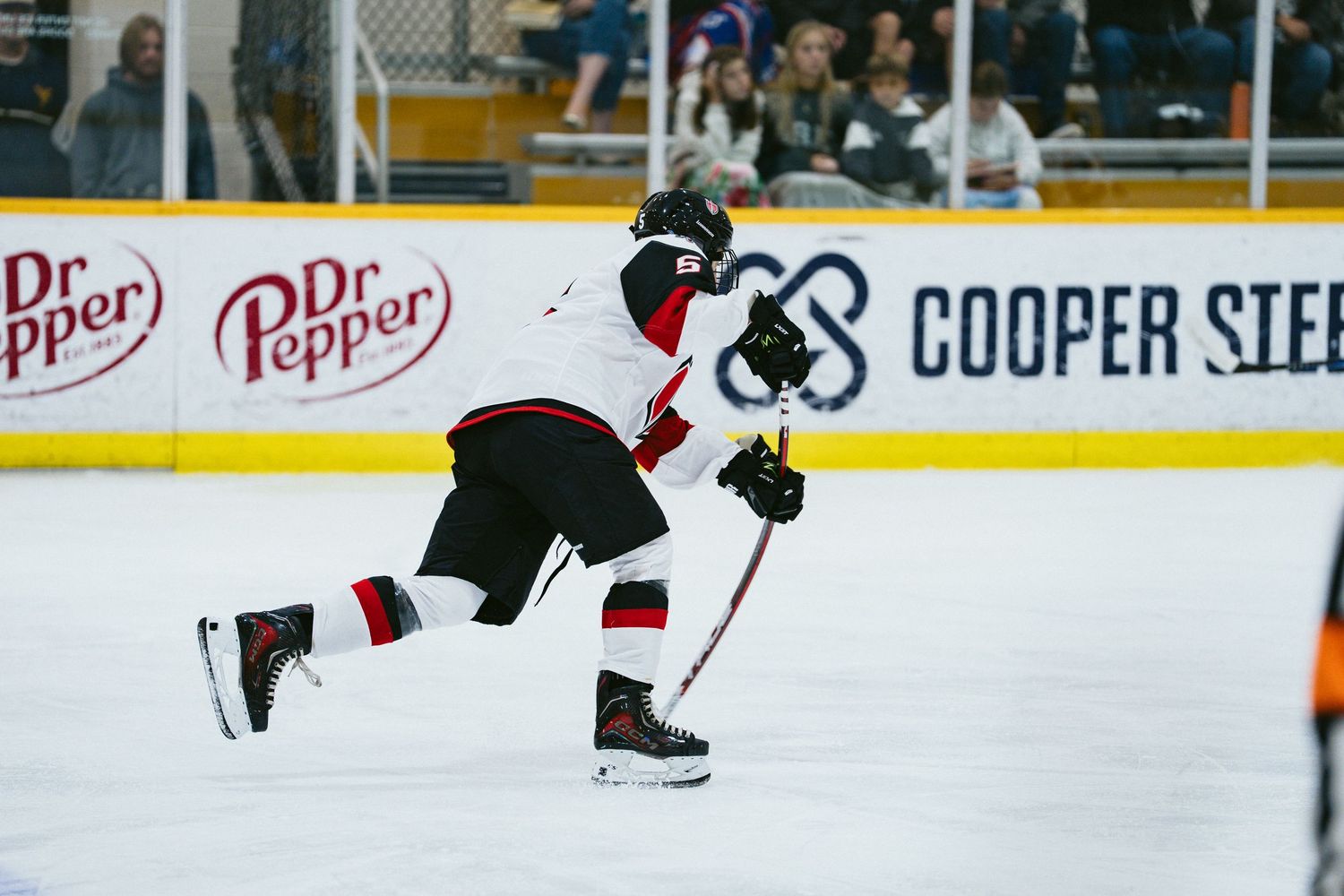 Ice hockey player in black and red uniform takes a powerful shot on the rink.