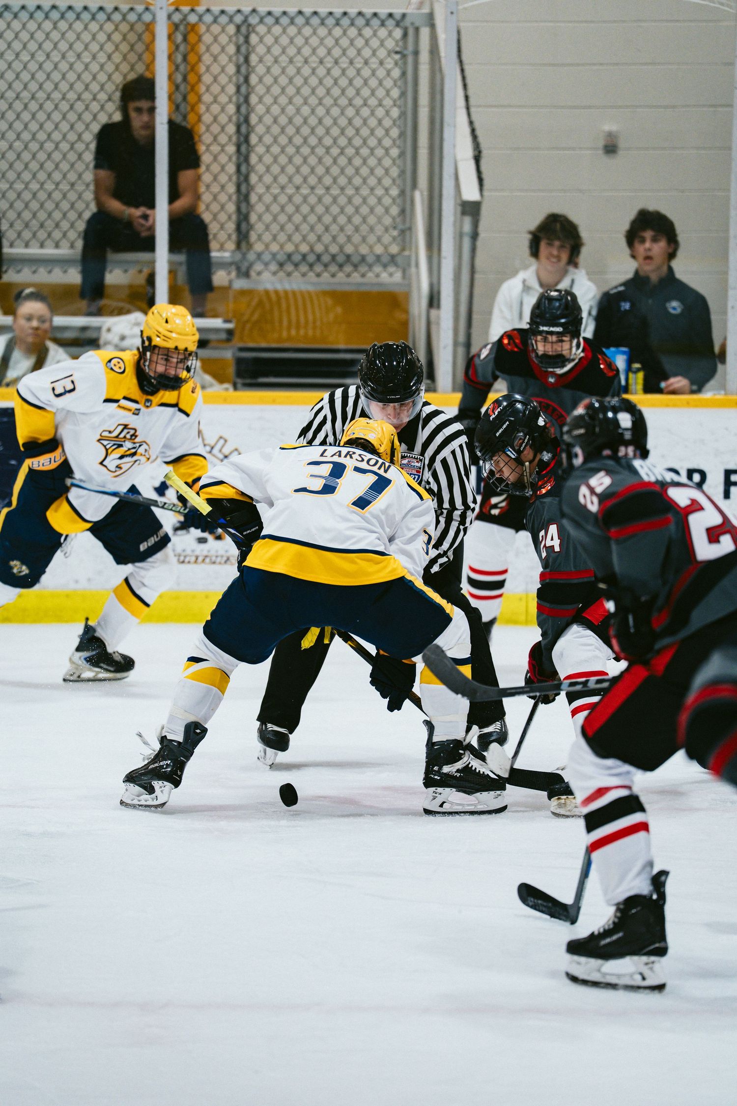 Youth hockey players face off at center ice as a referee drops the puck during an indoor hockey game.