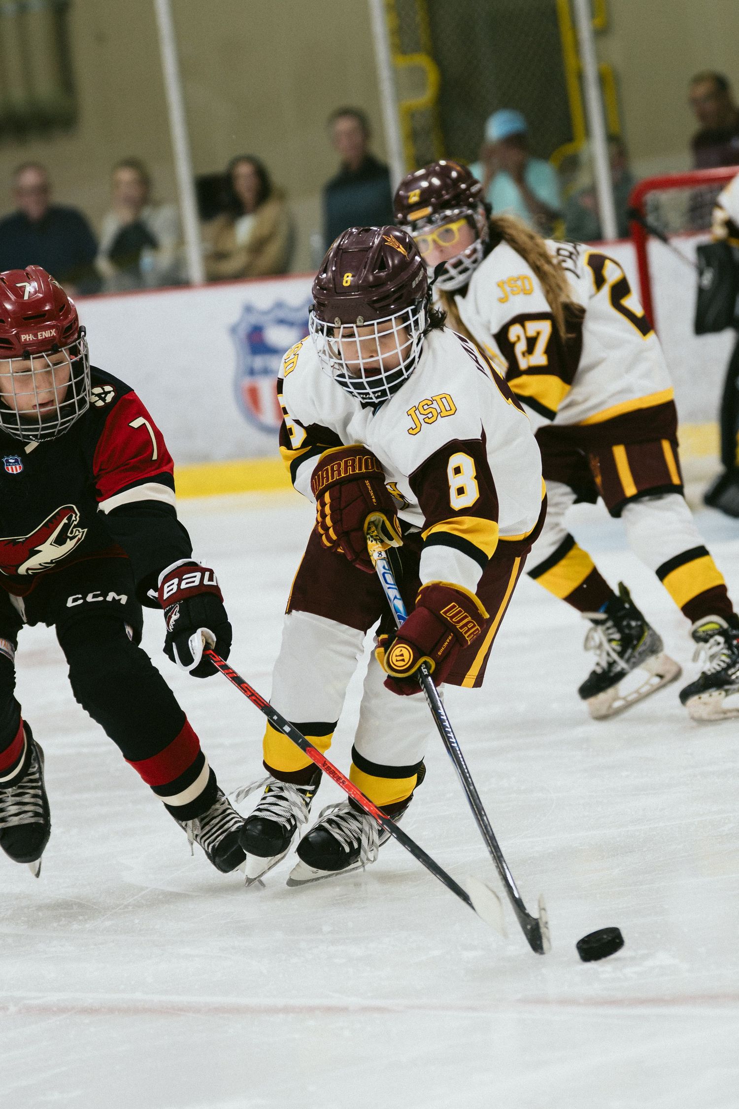 Female ice hockey player number 8 in white JSD uniform controls puck during competitive game on indoor rink.