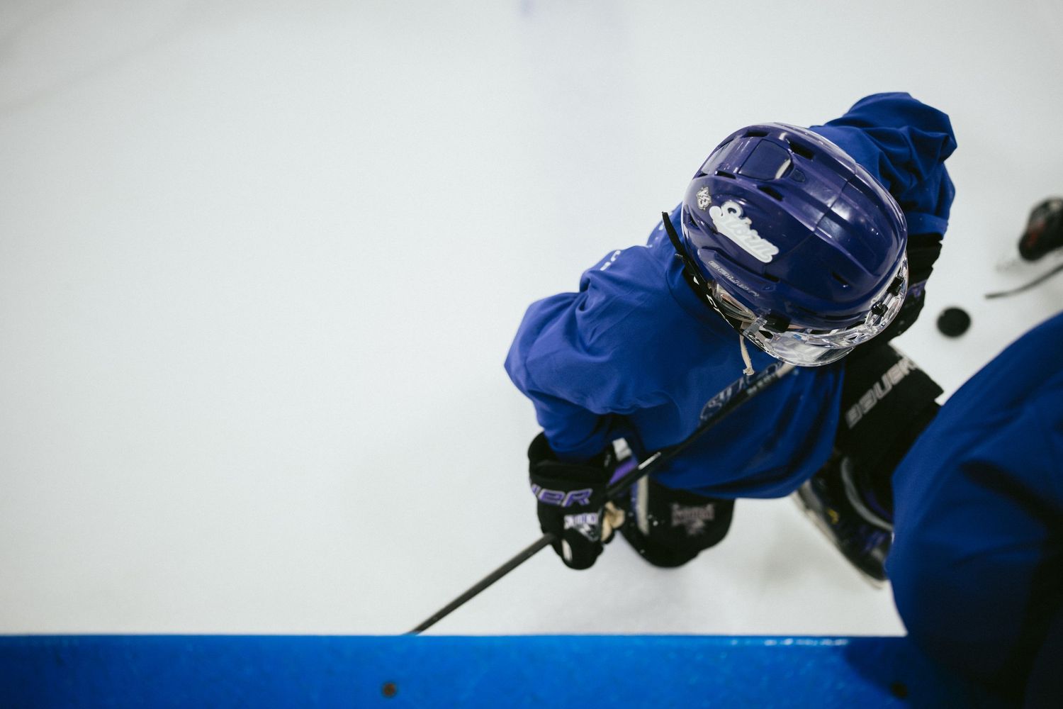 Aerial view of a young hockey player in blue uniform and helmet skating on ice rink during practice.