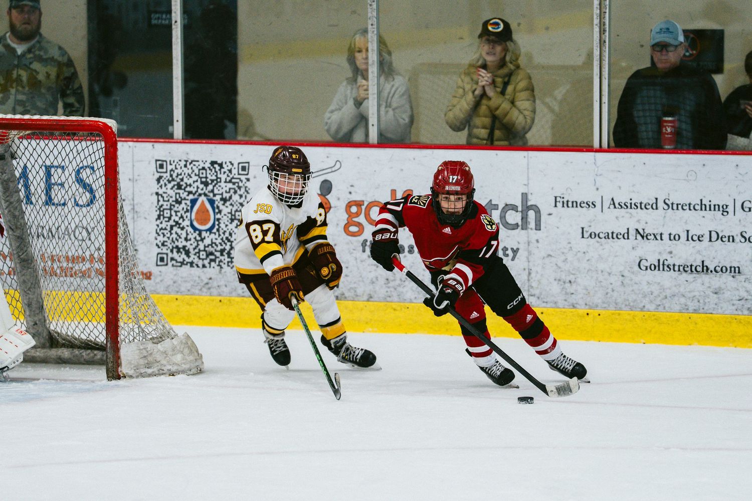 Two youth hockey players from opposing teams race for the puck during an intense game.