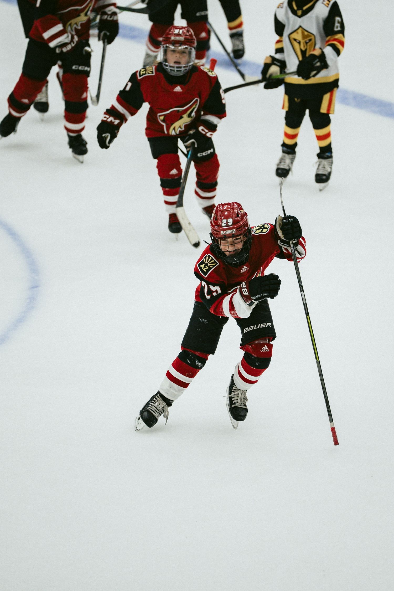 Youth hockey players in red and black jerseys compete for the puck during an intense game.