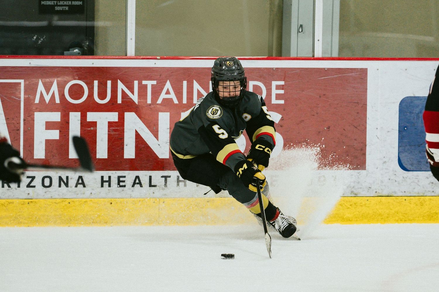 Hockey players in dark uniforms chase after the puck near the boards.
