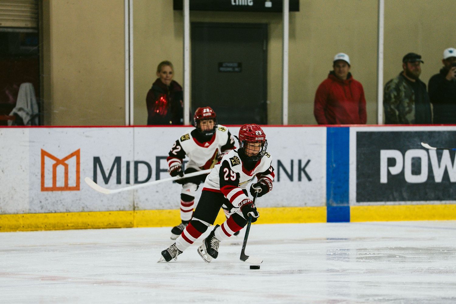 Hockey players skate on an ice rink during a competitive match with advertising boards visible in the background.