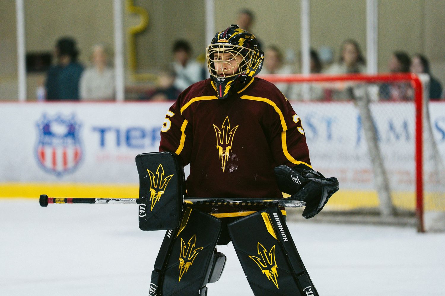 Hockey player in brown and gold uniform skating with stick on ice during game.